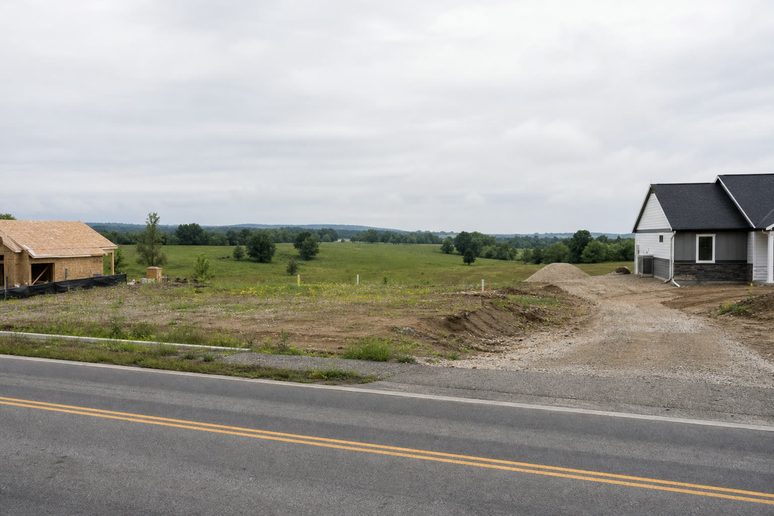 New homes and open land beside a two-lane county road.